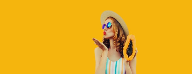 夏季肖像的年轻女子模特与新鲜木瓜水果摆姿势戴草帽，太阳镜在黄色背景图片下载