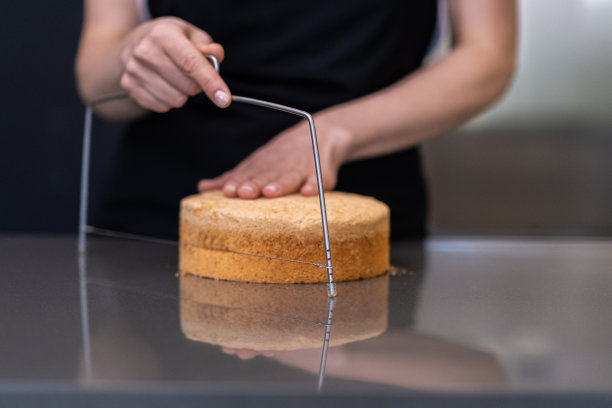 穿着黑色围裙的专业糖果师正在用刀切蛋糕图片下载