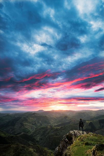 一个人站在一个郁郁葱葱、长满草的小山上，望着远处雄伟的山脉图片下载