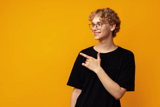 英俊的年轻人用手指指向黄色横幅背景上的复制空间图片下载