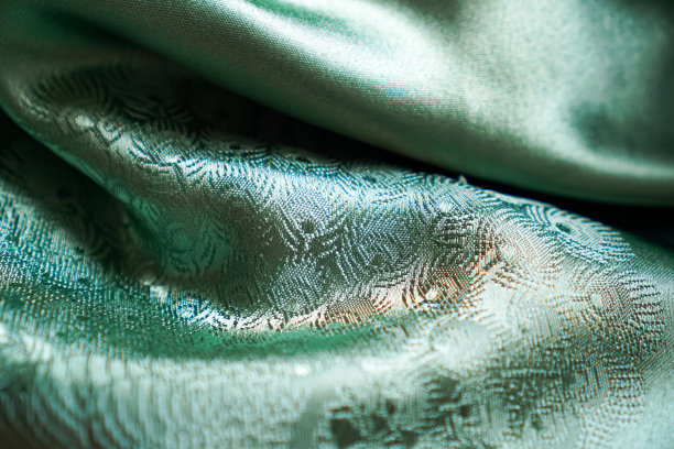 这张照片显示了翠绿色丝绸缎的反光折痕，图案漂亮，光线渐变。图片下载