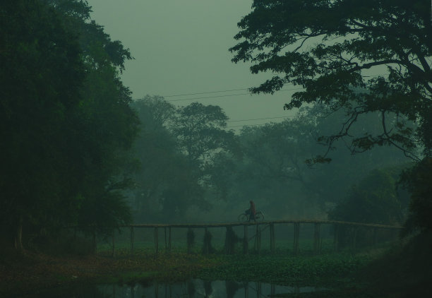 一个人扛着自行车，在下雨天独自走过一座吊桥。图片下载