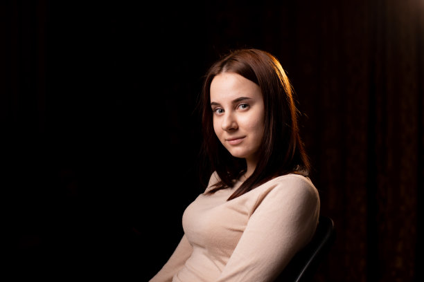 一个年轻女子在黑色背景上的肖像。穿棕色毛衣的那个女孩。友好的脸看着镜头。图片下载