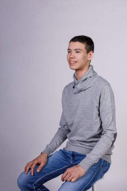 迷人的十几岁男孩坐在白色的背景下，自信地微笑着图片下载