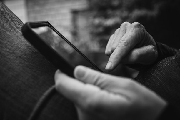 一个穿着休闲牛仔裤坐在户外长凳上看智能手机的人的特写。旅游，联系，放松，工作，在线，电子工作，远程工作概念。黑白复古照片。图片下载