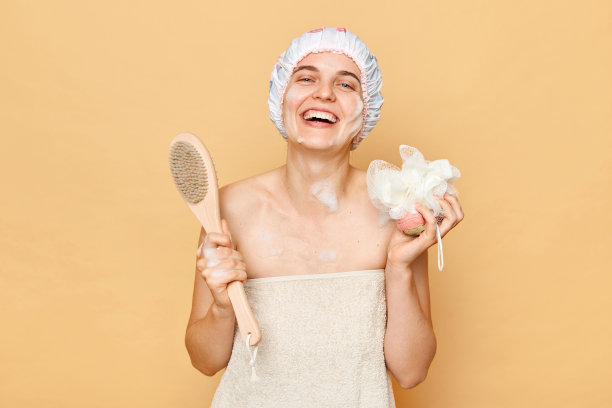 迷人、快乐、开朗的女人在浴室淋浴，拿着毛巾和身体刷进行磨砂和按摩，开心地笑着享受皮肤护理程序。图片下载