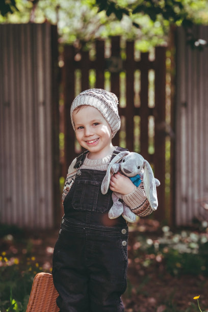 一个4岁的小男孩带着一个手提箱和一只毛绒兔子在户外旅行。一个孩子在街上玩耍的美丽画像。图片下载