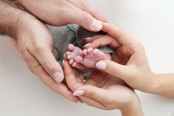 父亲的手掌，母亲的脚都抱着刚出生的婴儿在白色的背景。新生儿的脚放在父母的手掌上。孩子的脚趾、脚后跟和脚的照片。图片下载