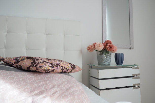 卧室室内设计。镜子在墙上。卧室里白色的桌子上放着一束漂亮的粉红色的花。室内设计。床与白色软垫床头板。装饰的枕头图片下载