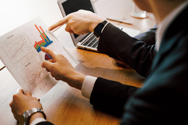 两个男人指着办公室会议桌上的材料和笔记本电脑图片下载