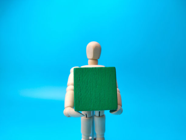 木制的人体模型拿着一个绿色的木头立方体，上面有一个空白的空间图片下载