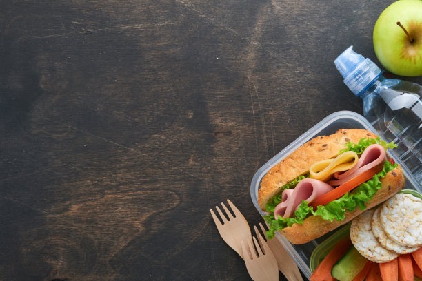 学校午餐的健康食品概念。健康面包，肉三明治，奶酪，苹果，新鲜黄瓜，胡萝卜，坚果在容器里，水和酸奶在黑暗的背景。回到学校的概念。图片下载