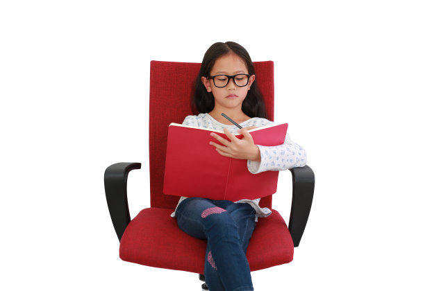 亚洲小女孩的肖像，坐在白色背景的红色织物椅子上，在书上写字。图像与剪辑路径图片下载