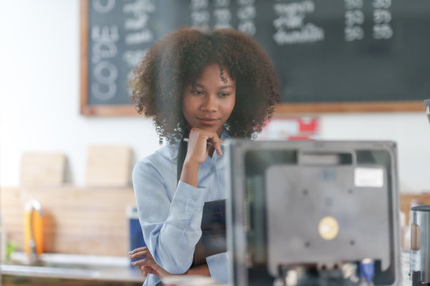 成功的年轻咖啡师，站在咖啡厅吧台的女人。小创业的业主概念。快乐的咖啡店女服务员系着围裙，在咖啡馆里自信地微笑着。图片下载