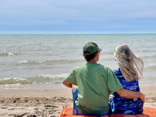 沙滩上坐在橙色毯子上的老年夫妇的后景图片下载