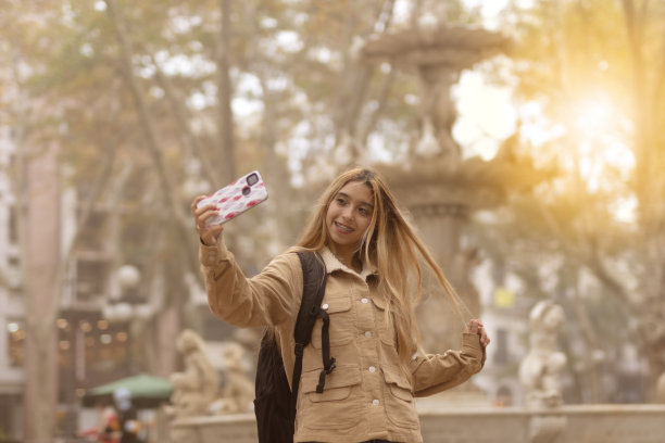 年轻的女游客在以喷泉为背景的城市广场自拍。图片下载