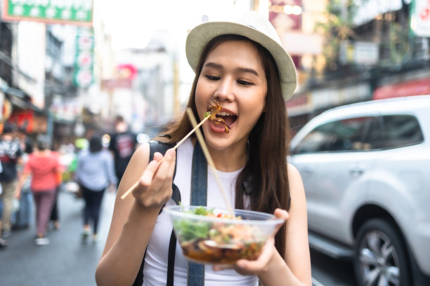 年轻的成年亚洲吃货女背包旅行者在唐人街街头小吃吃亚洲甜点。旅游女孩们正在享受曼谷美丽的地方。图片下载