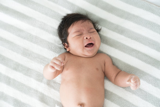 新生婴儿在白色的床上盖着毯子睡觉时啼哭。亚洲新生儿啼哭图片下载