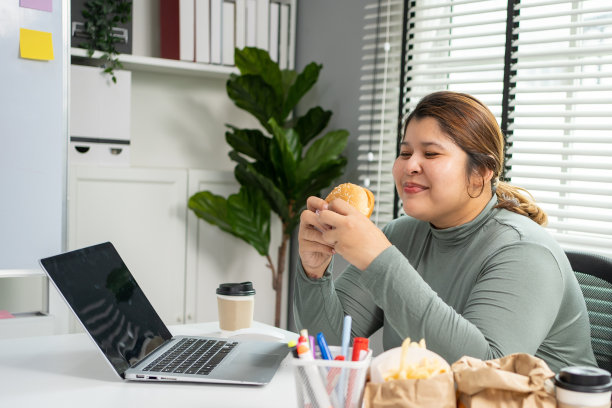 亚洲女人在办公室吃汉堡。图片下载