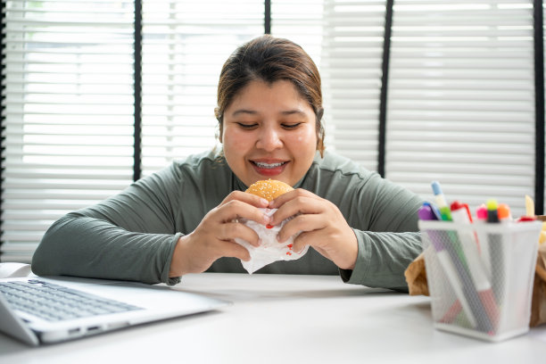 亚洲女人在办公室吃汉堡。图片下载