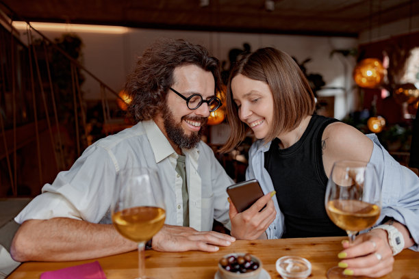一对相爱的微笑情侣在酒吧喝酒时看着手机上的照片图片下载