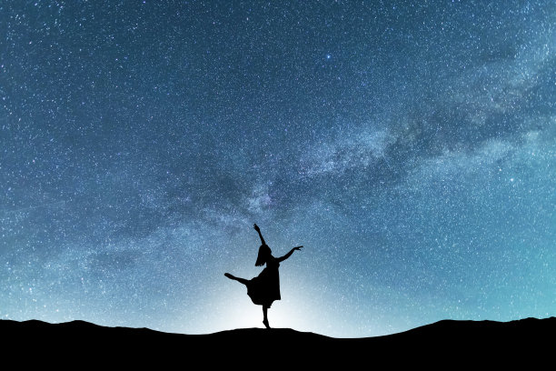 女人的剪影在夜晚跳舞，在明亮的银河背景上。图片下载