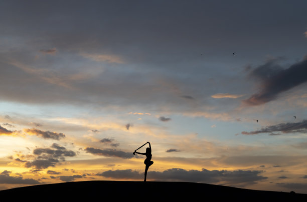 女人的剪影在明亮的夕阳天空背景上跳舞。图片下载