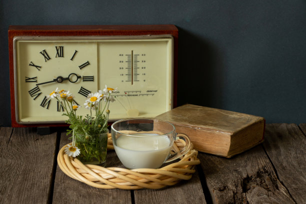 一杯牛奶，一只插着雏菊的花瓶，钟旁边，厨房的木桌上放着一本书图片下载