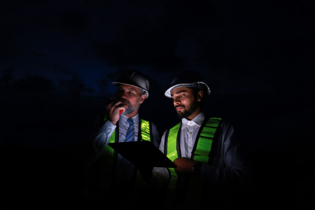 专业工程师晚上在现场一线辛勤工作。高级经理和他的工程师穿着安全背心和个人防护装备，带着笔记本电脑和对讲机在晚上工作图片下载