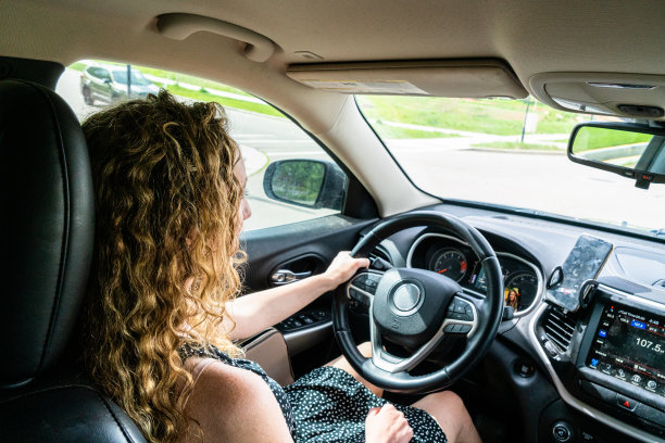 一个年轻的女人，一头飘逸的金色卷发，穿着长及膝盖的带有白点的黑色连衣裙，开着她的SUV，一边用免提设备无缝地聊天。图片下载