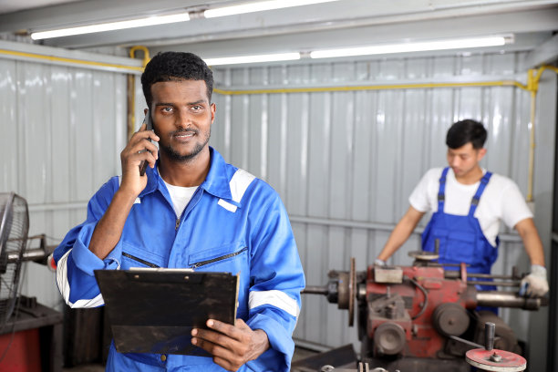 在车库，多民族技师技师使用金属车床用智能手机和剪贴板操作抛光汽车盘式制动器。维护汽车和检查汽车零件的概念图片下载
