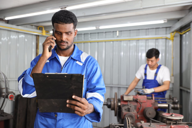 在车库，多民族技师技师使用金属车床用智能手机和剪贴板操作抛光汽车盘式制动器。维护汽车和检查汽车零件的概念图片下载