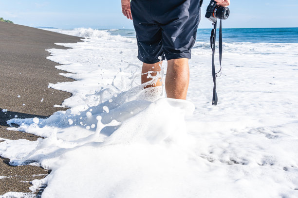 一个人拿着相机沿着海水走图片下载