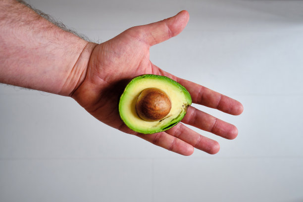 一个男人手里拿着一个绿色的鳄梨。鳄梨特写。天然新鲜有机外来水果。健康饮食，生食饮食。素食者的生活。适当的营养。可以吃了。生态产品。海报图片下载