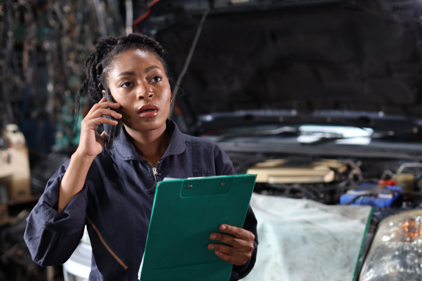 一名穿制服的女技师在修车站用智能手机拿着剪贴板检查汽车维修服务。汽车维修服务理念图片下载