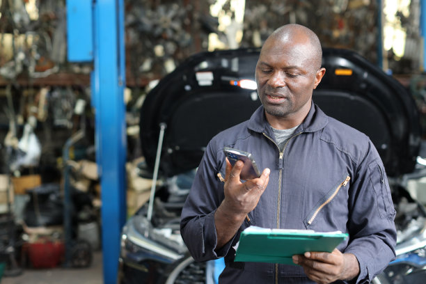 在修车站，穿着制服的汽车技师一边用智能手机一边用平板电脑检查汽车维修服务。汽车维修服务理念图片下载