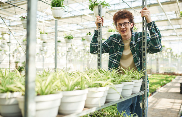 穿着格子衬衫。一个戴眼镜的卷发年轻人在温室里图片下载
