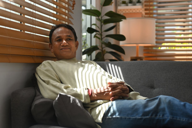 照片中，一位穿着长袖毛衣的亚洲老人坐在沙发上，看起来很放松。图片下载