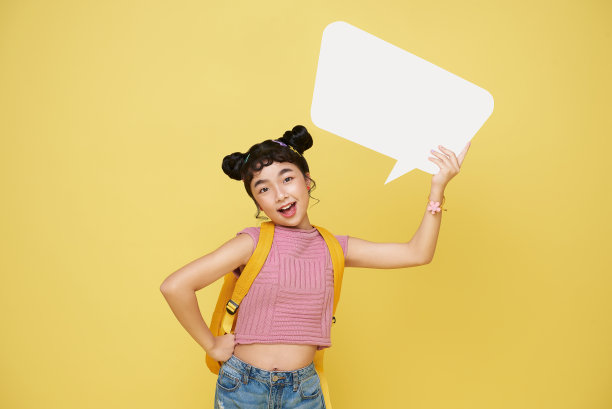 快乐微笑的亚洲女学生举着一个空的白色演讲泡，孤立在黄色的工作室背景上。图片下载