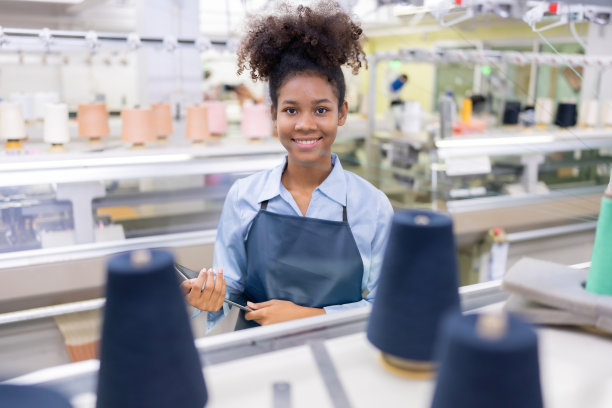 美国女设计师，织布者手持牌匾站着，送出一个可爱的微笑。前面有一台缝纫机和线盘。在一个大型的缝纫行业图片下载