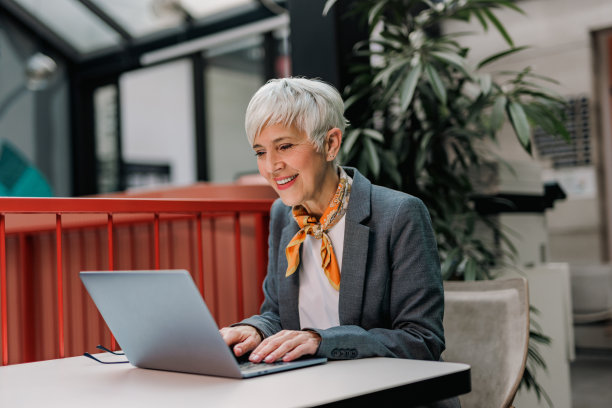 高级商务女性在线工作，在办公室，独自坐着，使用笔记本电脑。图片下载