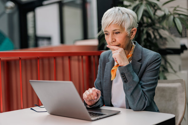 高级女性坐在办公室，用笔记本电脑工作。图片下载