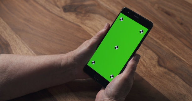 老女人的手在木桌上拿着绿屏的智能手机图片下载