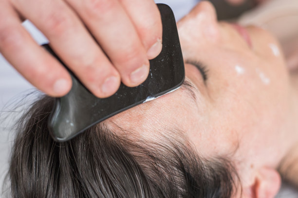 年轻的白人女性正在做面部护理。治疗师正在做刮皮术。中医手法，瓜沙，止痛，治疗，活血。刺激疗法。图片下载