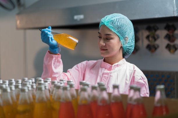 亚洲女工在饮料厂检查产品瓶子的质量，传送带上的罗勒籽和水果。制造商和检验质量控制图片下载