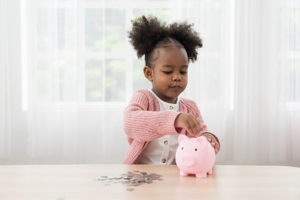 储蓄和银行理财的概念。小女孩往储蓄罐里存钱。非洲裔美国小女孩把一枚硬币放进存钱罐里。儿童投资未来概念图片下载