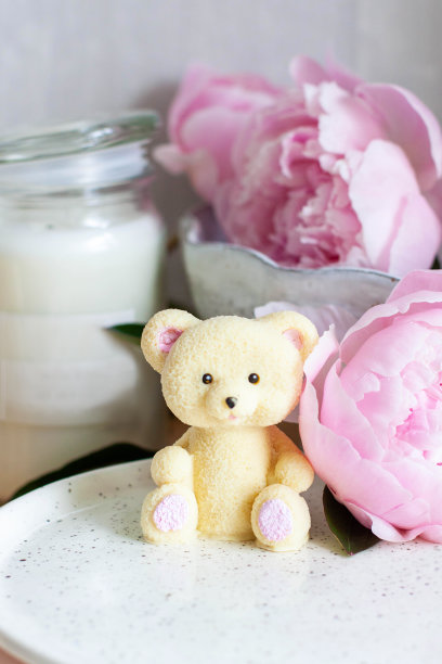 可爱的可食用的泰迪熊玩具由白巧克力和新鲜的牡丹和蜡烛的背景。给宝宝的礼物图片下载
