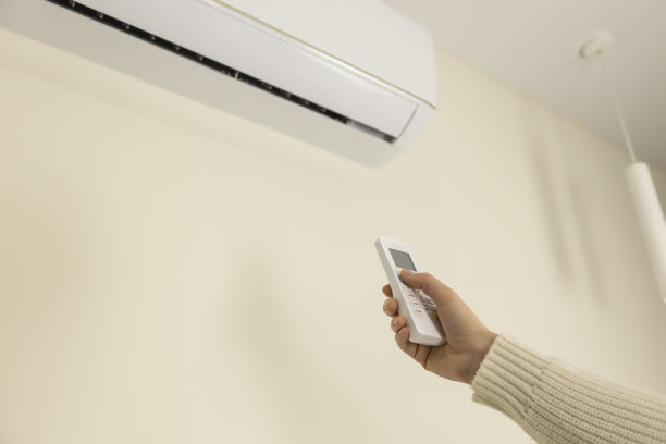一个人手里拿着一个白色的空调遥控器，目的是打开空调，调节房间里的空气温度图片下载