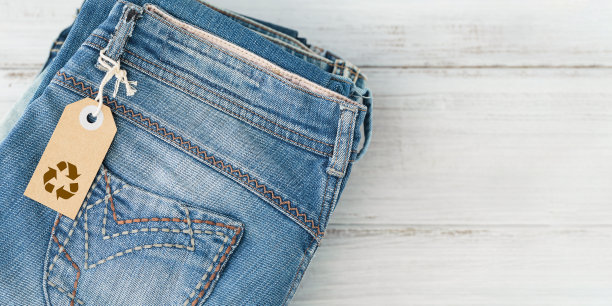 一叠蓝色牛仔裤和带有回收标志的手工纸标签图片下载