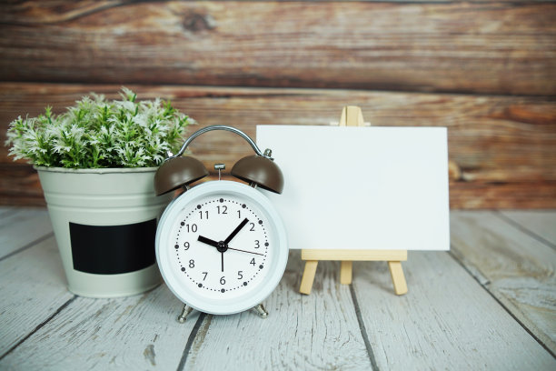 空卡模型与人工植物和白色闹钟在木制背景图片下载